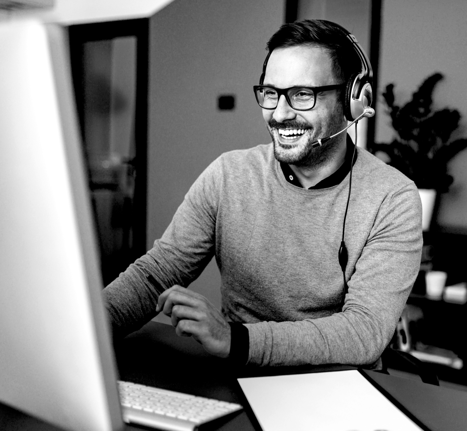 Photo en noir & blanc, homme souriant travaillant devant un ordinateur et avec un casque audio
